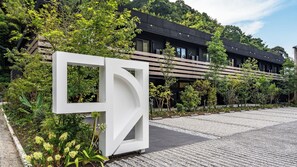 A modern building with a geometric entrance, surrounded by lush greenery and a paved walkway. - 1HOTEL (Shizuoka)