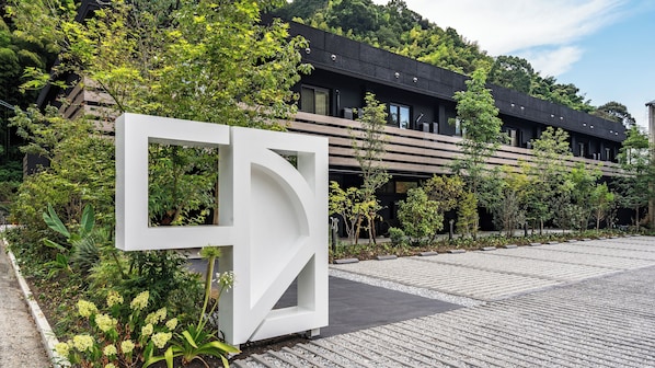 A modern building with a geometric entrance, surrounded by lush greenery and a paved walkway.