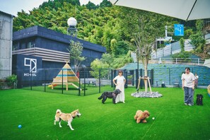 A fenced outdoor area with artificial grass, a playground, and a building with a satellite dish. - 1HOTEL (Shizuoka)