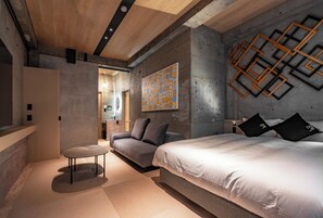 A modern bedroom with a large bed, a sofa, a small round table, and a geometric wall art piece. - 1HOTEL (Shizuoka)