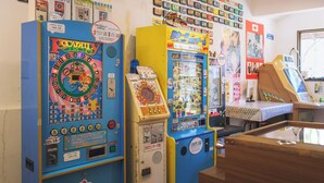 A row of arcade machines, including a 'Piccadilly Circus' game, in a room with various posters and a wooden counter. - 1HOTEL (Shizuoka)