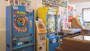 A row of arcade machines, including a 'Piccadilly Circus' game, in a room with various posters and a wooden counter. - 1HOTEL (Shizuoka)