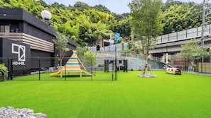 A hotel with a modern design, a children's play area, and a lush green lawn. - 1HOTEL (Shizuoka)
