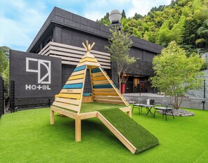A hotel with a modern black facade, a wooden play structure, and a grassy lawn. - 1HOTEL (Shizuoka)