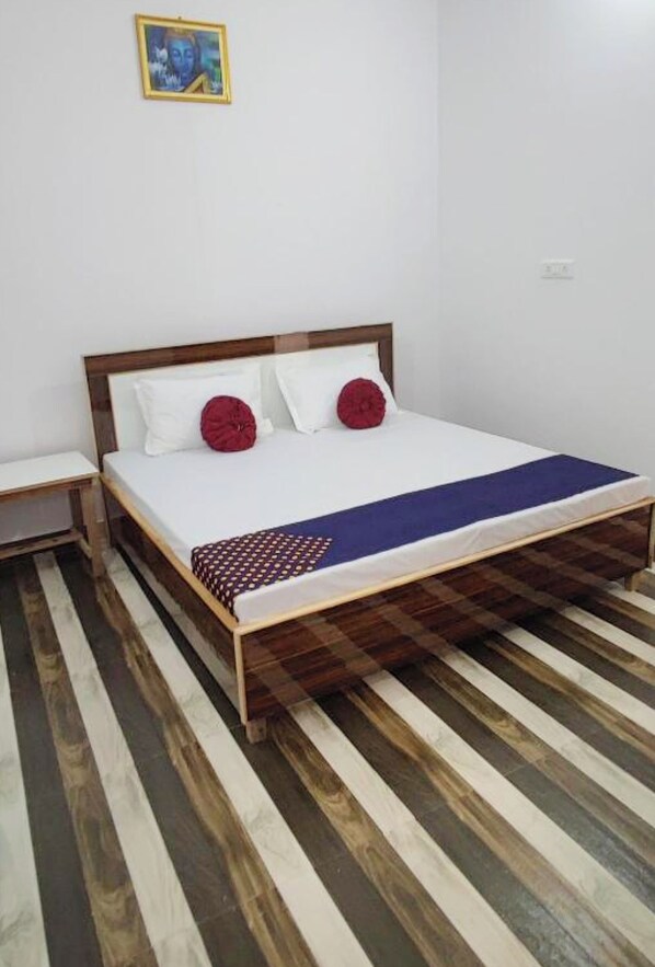 Una cama individual con estructura de madera, ropa de cama blanca y dos almohadas rojas.
