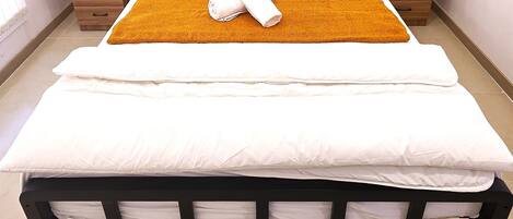 A neatly made bed with white linens, a brown throw blanket, and a folded towel. There are two wooden nightstands with drawers, one on each side of the bed.