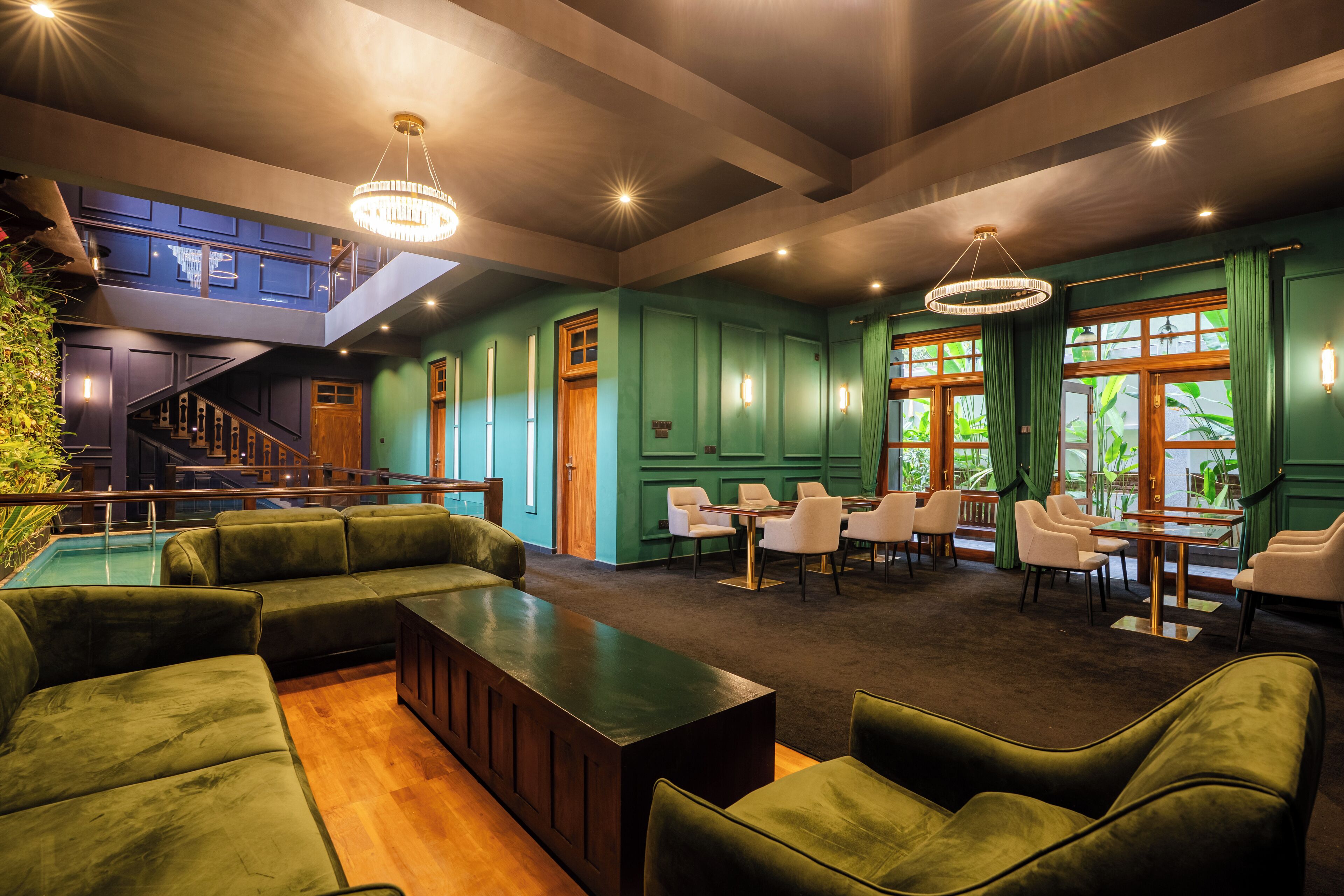 A spacious lounge area with green upholstered seating, a wooden reception desk, and a staircase leading to an upper level.