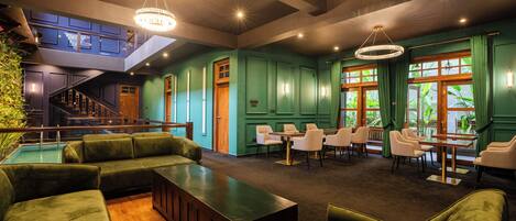 A spacious lounge area with green upholstered seating, a wooden reception desk, and a staircase leading to an upper level.