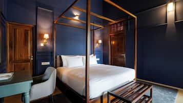 A four-poster bed with white linens, a wooden desk with a chair, and two wall-mounted lamps.