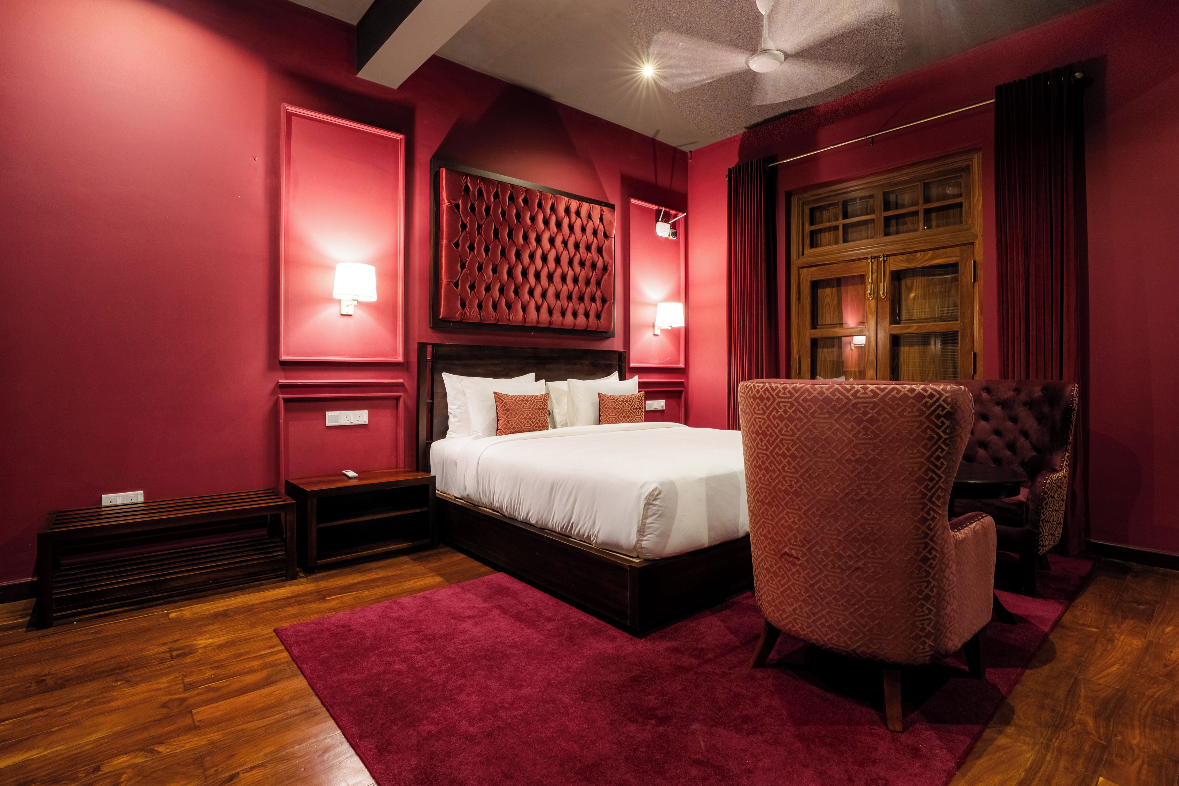 A bedroom with a large bed, a wooden headboard, a red accent wall, a red rug, and a chair.