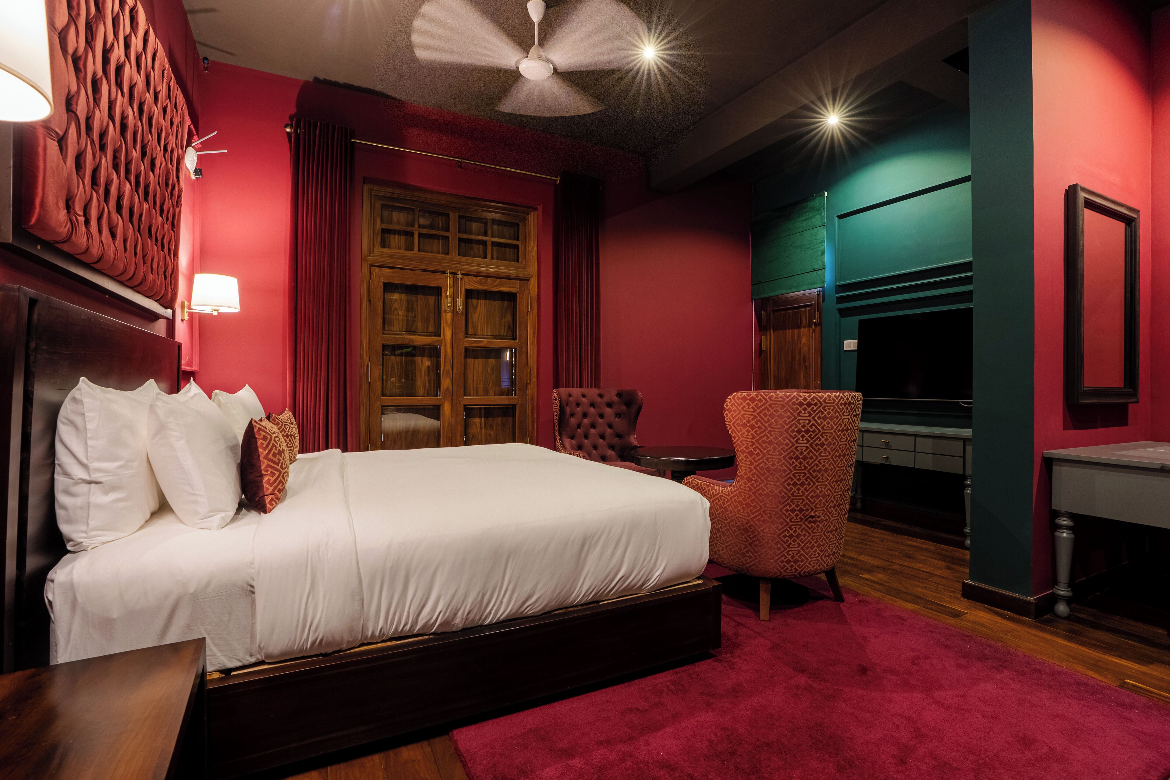 A hotel room with a large bed, a sitting area with a chair, a television, and a wooden door.