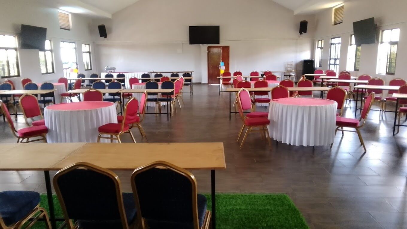 Uma sala de conferências com fileiras de mesas e cadeiras, grandes janelas e um palco.
