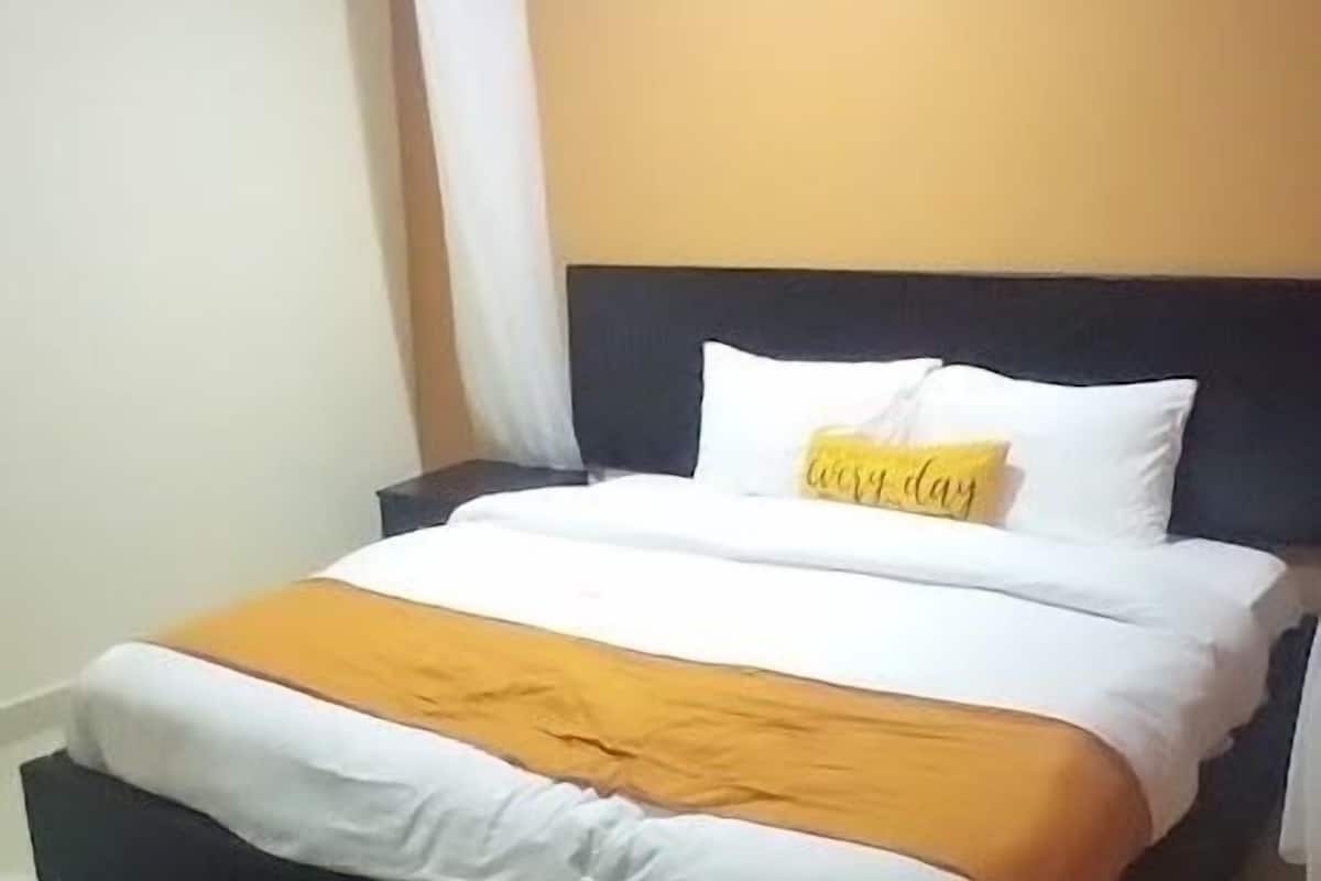 A neatly made bed with white and orange bedding, a black headboard, and a single yellow pillow with the text "every day".