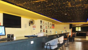 A bar area with a counter, chairs, a ceiling with a starry design, a fan, and a computer monitor.