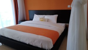 A bed with white and orange bedding, a black headboard, and a pillow with text.