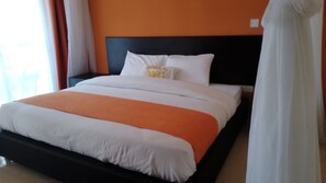 A bed with white and orange bedding, a black headboard, and a pillow with text.