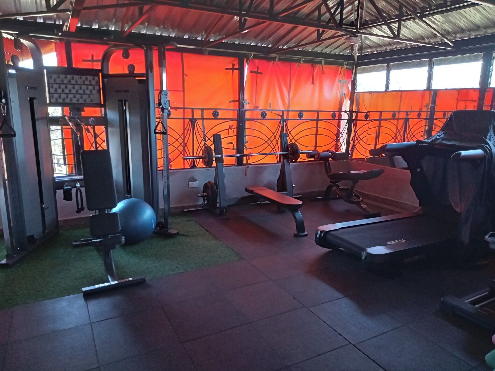 Een sportschool met diverse fitnessapparaten, waaronder een loopband, een gewichtbank en trainingsballen.
