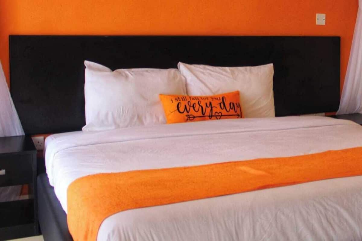 A bed with white and orange bedding, a black headboard, and a pillow with text.
