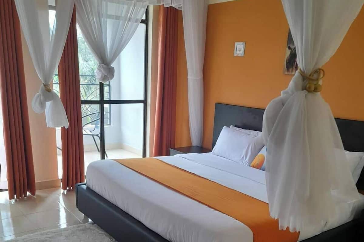 A hotel room with a large bed, white curtains, and a view of the outdoors.