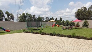 A paved patio area with a playground featuring a slide and swings. - Darrel Paradise Resort (Bungoma)