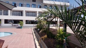 A building with a swimming pool, outdoor seating, and a garden area with palm trees. - Darrel Paradise Resort (Bungoma)