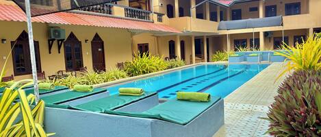 A swimming pool with lounge chairs and a covered area with a mesh roof.