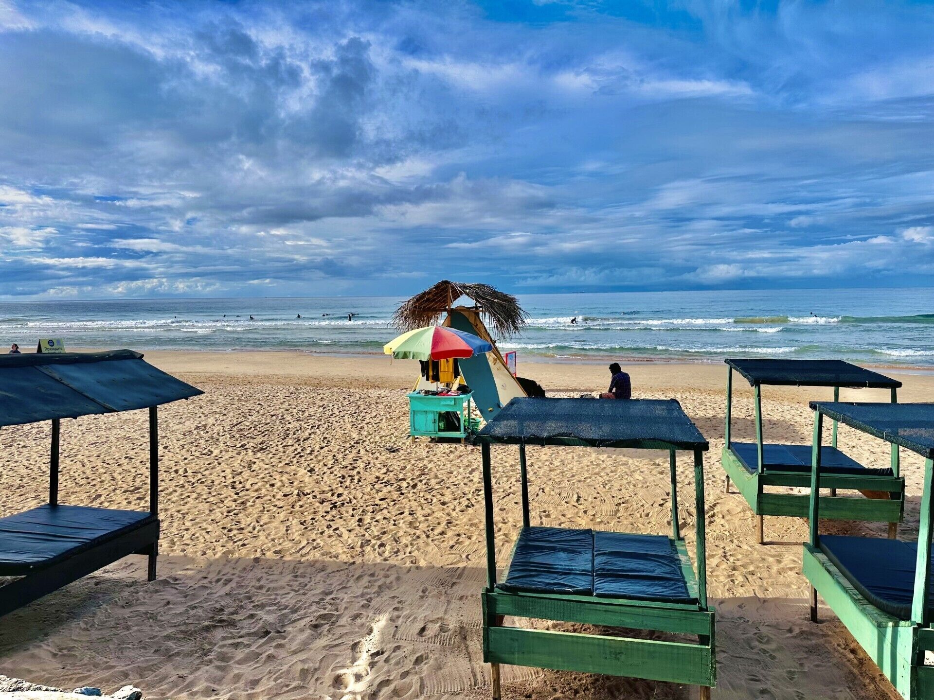 A beach with a row of green beach chairs and a colorful umbrella.