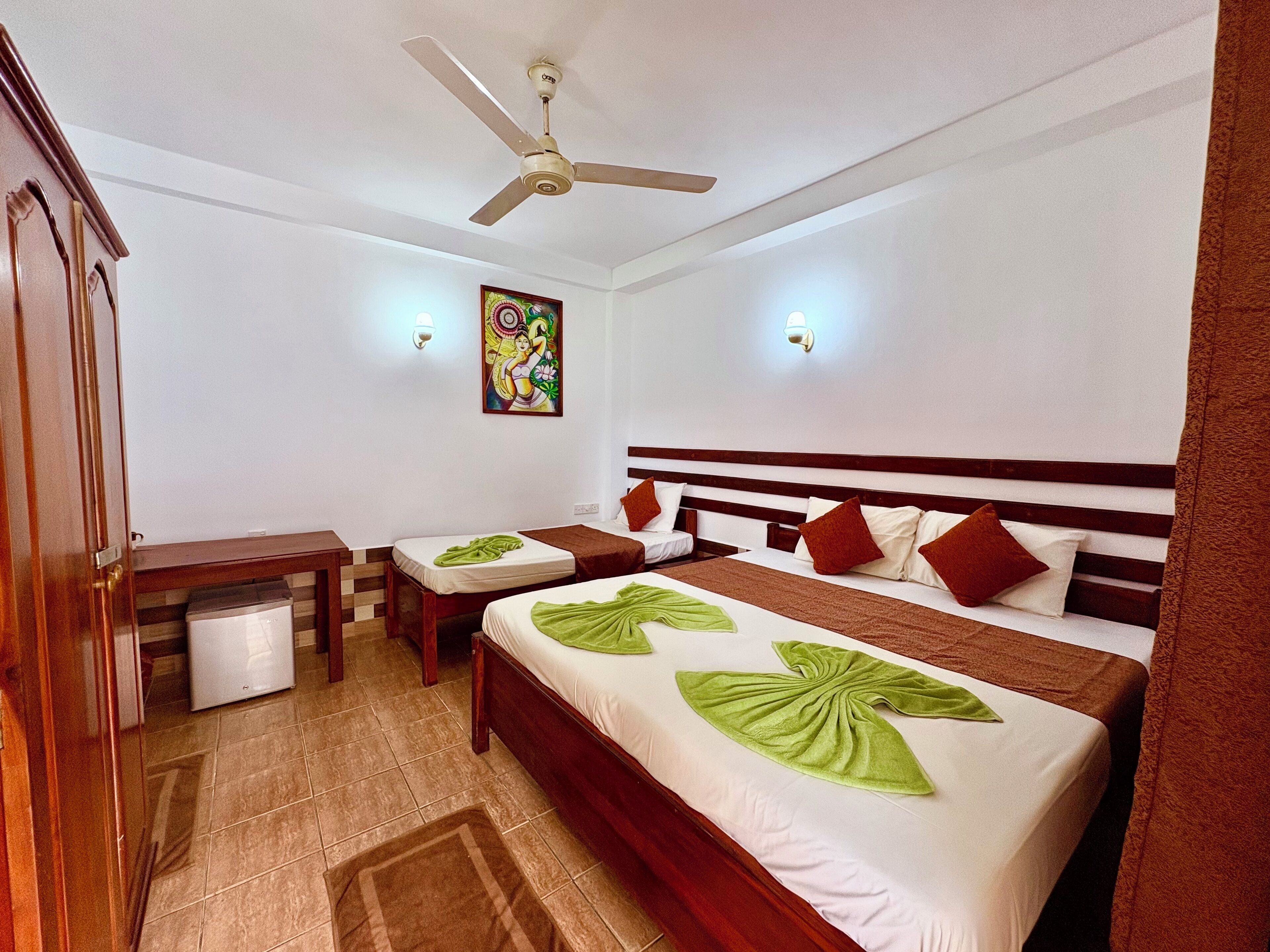 A hotel room with two beds, a ceiling fan, a small table, and a trash bin.