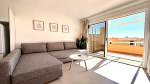 A living room with a grey sectional sofa, a small round table, and three framed pictures on the wall.