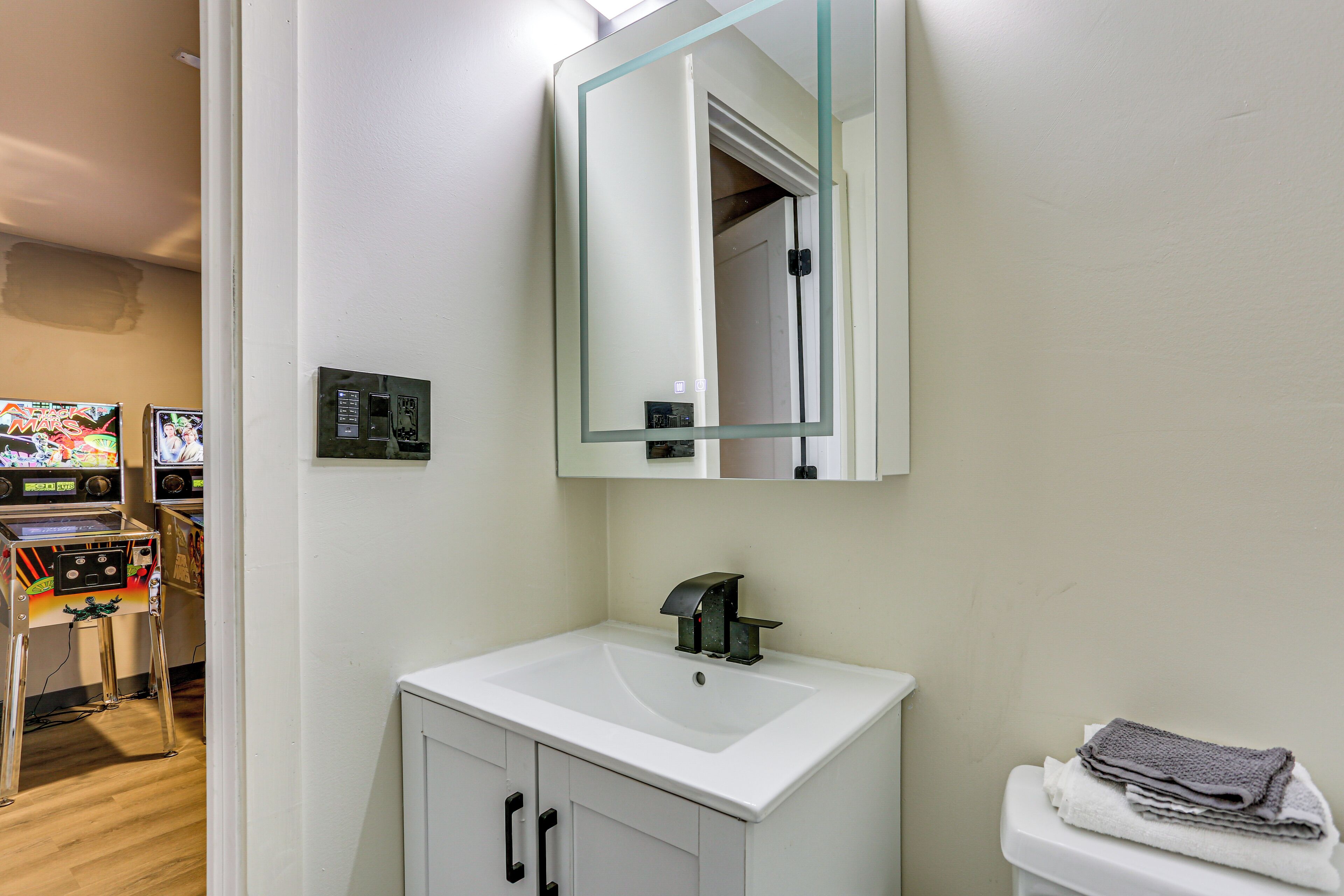 Een badkamer met een wit wastafel, een spiegel en een toilet. Daarboven hangt een klein kastje met een spiegel.