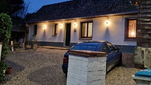 Ett hus med en grusuppfart, en parkerad bil och en väl upplyst fasad.