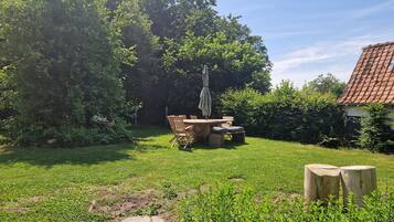 Een tuin met een houten tafel en stoelen, omgeven door weelderige begroeiing en bomen.