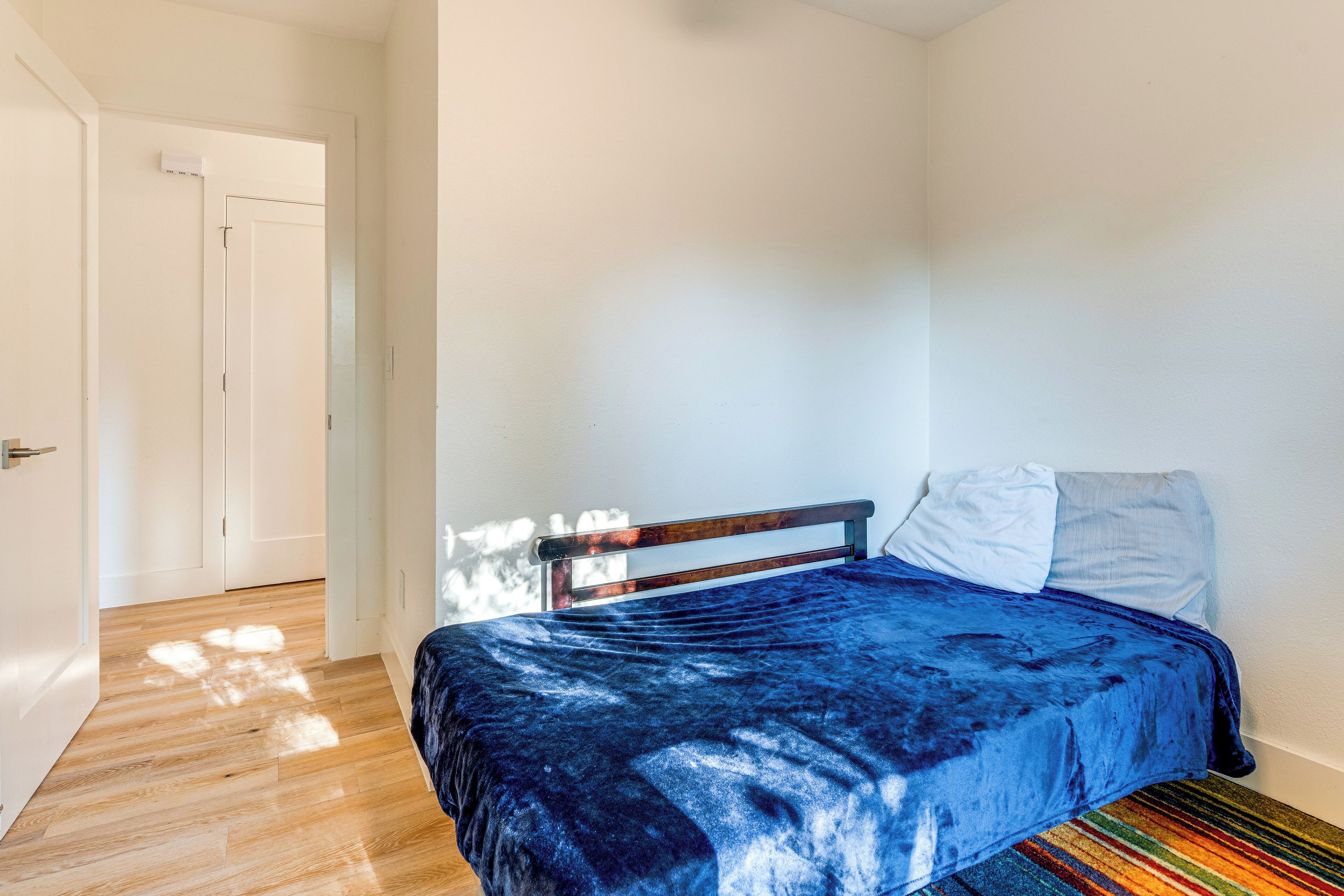 Un dormitorio con cama, cabecera de madera, pared blanca y suelo de madera.