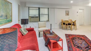 Ein Wohnzimmer mit einem roten Sofa, einem kleinen Tisch mit einer Vase und einem Essbereich mit Tisch und Stühlen.
