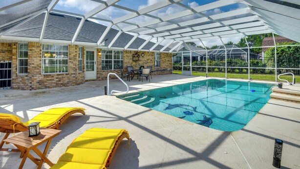 Une piscine intérieure dotée d’un toit en verre, de chaises longues jaunes et d’un bâtiment en briques en arrière-plan.
