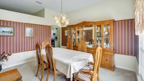 Une salle à manger comprenant une table, des chaises, un lustre et un buffet en bois doté de portes en verre.