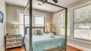 Una cama con dosel con un edredón azul acolchado, una mesita de noche de madera con cajones, dos lámparas de noche y una ventana con persianas.