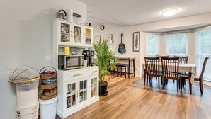 Uma área de refeições com mesa e cadeiras de madeira, uma planta em vaso e um armário branco com portas de vidro.