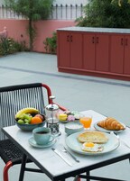 Uma mesa posta com itens de café da manhã, incluindo frutas, um croissant e uma xícara de café.