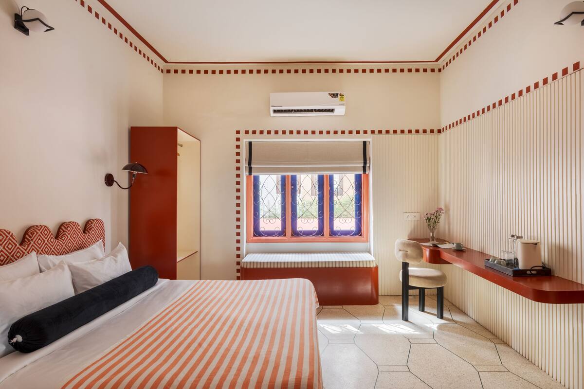 A hotel room with a bed, a bench, a desk, and a window with curtains.