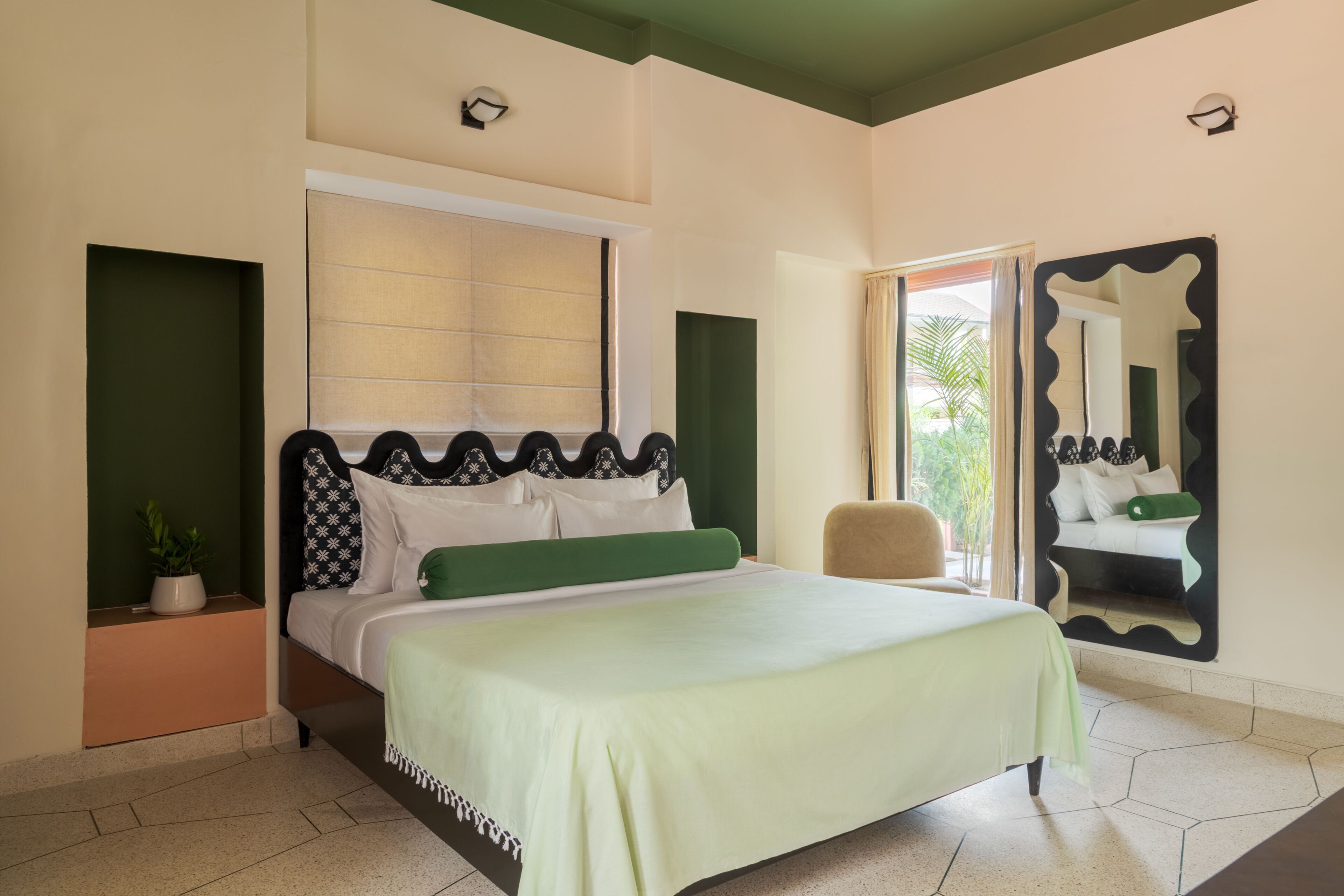 A bedroom with a bed, a potted plant, a chair, and a large mirror.
