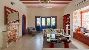 Uma sala de estar com sofá, poltrona e mesa de centro. Há estantes e uma janela com vista.