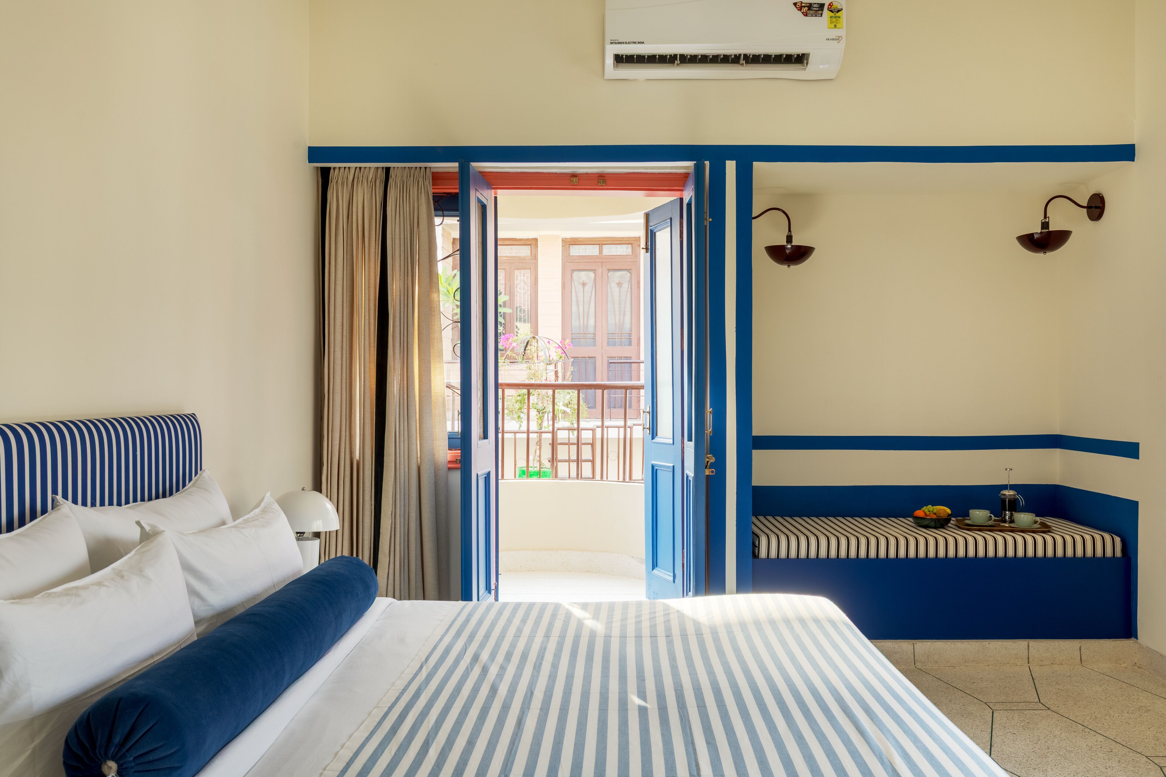 A hotel room with a bed, a window with curtains, a balcony, and a wall-mounted lamp.