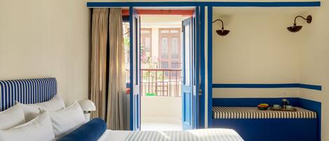 A hotel room with a bed, a window with curtains, a balcony, and a wall-mounted lamp.
