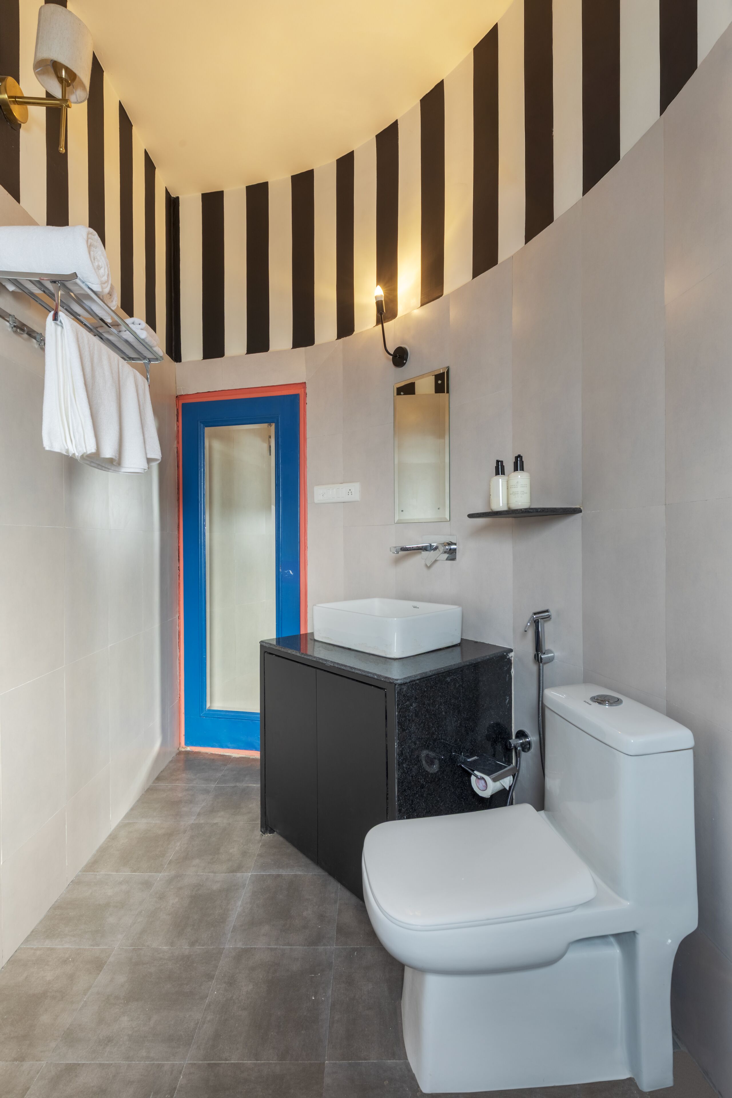 Un baño moderno con inodoro blanco, tocador negro, lavabo blanco y puerta azul.