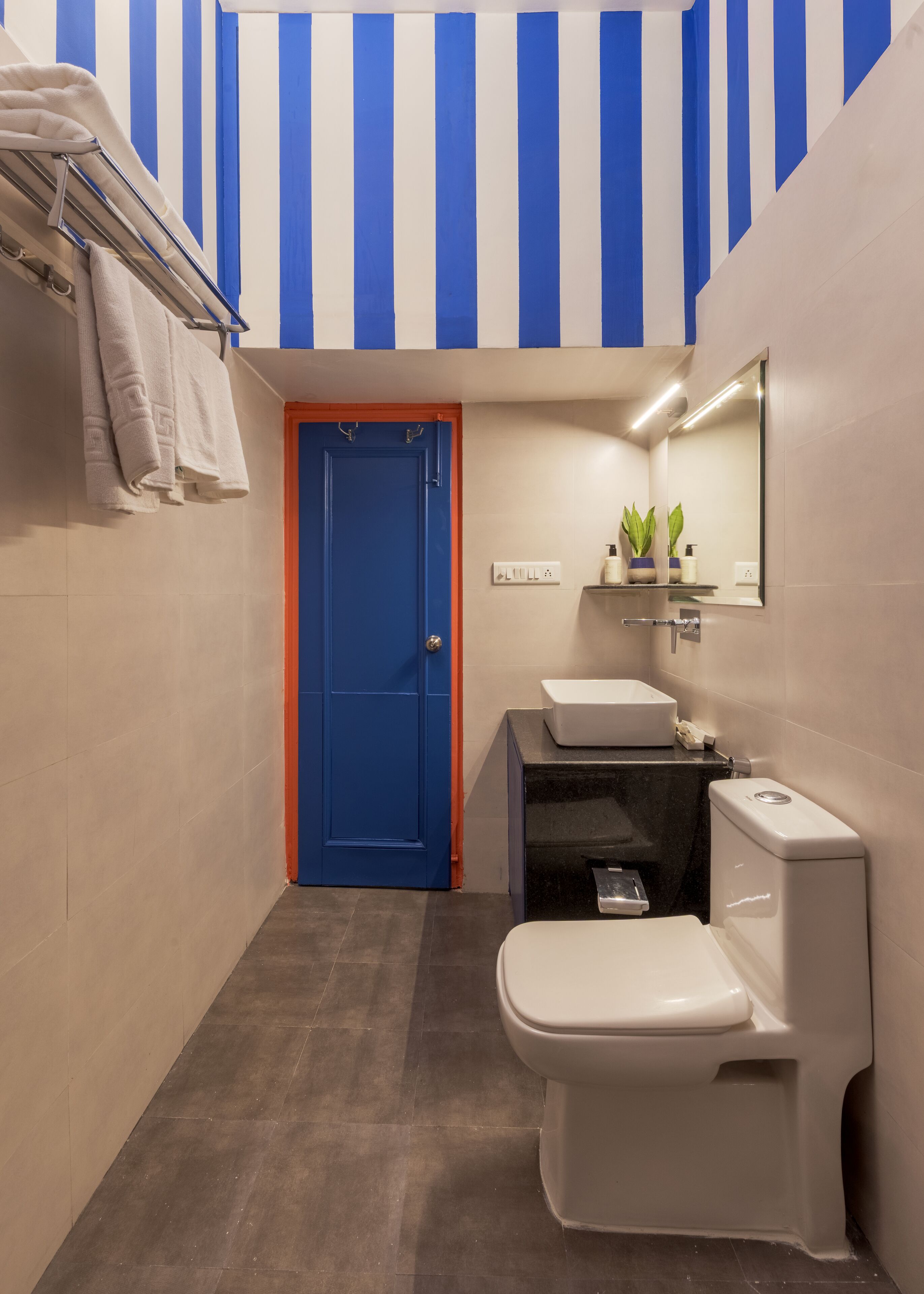 Casa de banho com porta azul, pia branca e espelho sobre a pia.