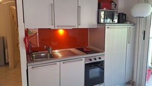A compact kitchen with white cabinets, a stainless steel sink, a built-in oven, and a small countertop with a kettle. - Seaside in Menton.2 rooms with balcony and parking. (Menton)