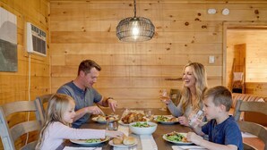 Comedor de madera con un candelabro, una mesa preparada para una comida familiar y una pared de madera con un equipo de aire acondicionado.