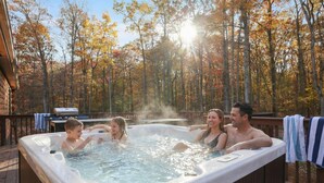 Un jacuzzi en una terraza de madera rodeado de árboles con follaje otoñal.