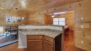 Interior de una cabaña de madera con cocina que incluye encimeras de granito, armarios de madera y una mesa de comedor con sillas.